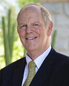 Tom O'Halleran standing outside wearing a dark suit and a light green tie, smiling