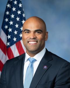 Collin Allred standing in front of an American flag with dark blazer, white button down and red tie