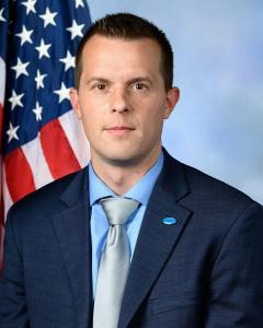 Jared Golden in front of an American flag in a blue suit and silver tie