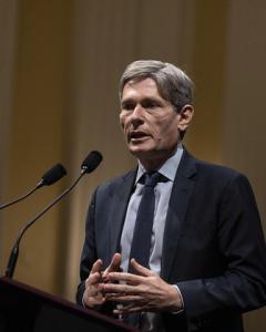 Tom Malinowski speaking at microphone in a grey shirt and black tie and jacket